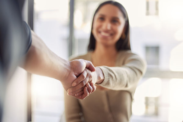 I woman is pictured in the background reaching out and shaking hands with someone in the foreground