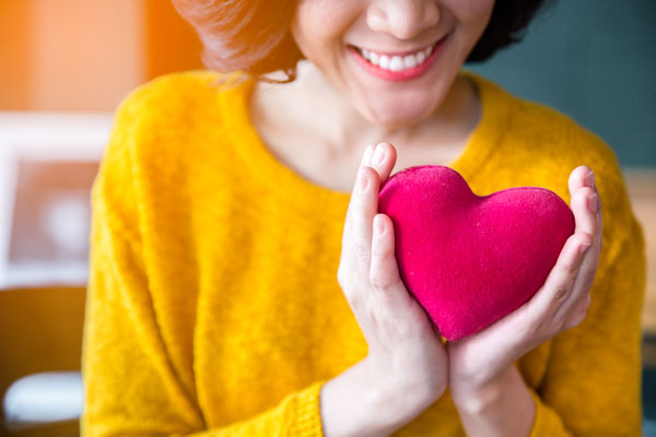 a woman in a bright yellow sweater craddling a red felt heart in her hands and smiling